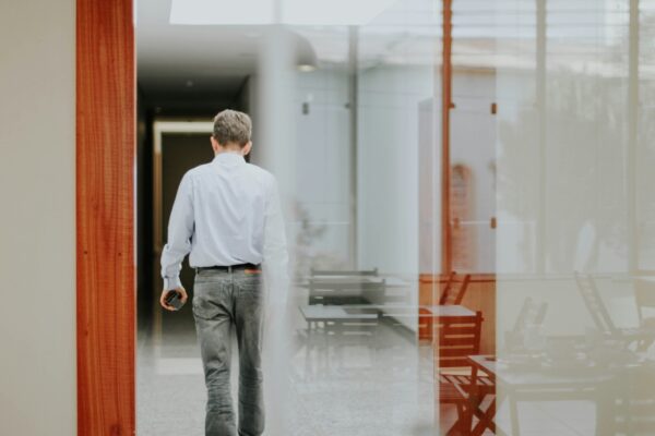 Man in a striped shirt walking away down a glass-walled office corridor